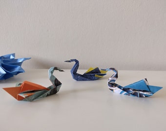 May include: Four origami swans made of patterned paper. Two swans are blue and white, one is orange and blue, and one is blue and yellow.