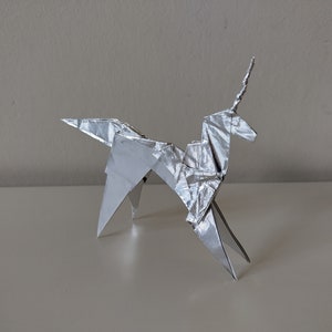 May include: A silver origami unicorn with a pointed horn, standing on a white surface.