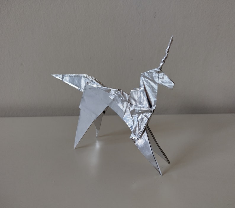 May include: A silver origami unicorn with a pointed horn, standing on a white surface.