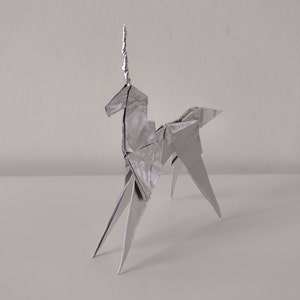 May include: A silver origami unicorn sculpture. The unicorn is standing on a white surface.