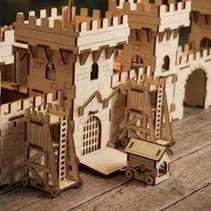 Puede incluir: Maqueta detallada de un castillo de madera con múltiples torres, una puerta y equipos de asedio. El modelo está hecho de madera de color marrón claro y presenta intrincados detalles recortados. El castillo está sobre una superficie de madera.