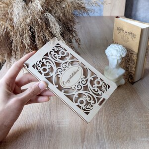 May include: A wooden card with a decorative cut-out design and the words "Congratulations!" engraved on the front.