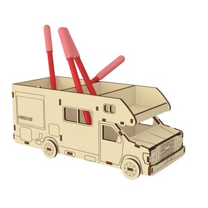 May include: A wooden desk organizer shaped like a camper van with three red pens sticking out of the top. The camper van is light brown with a white roof and windows.