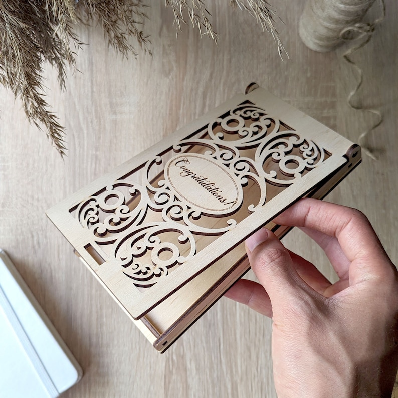 May include: A wooden box with a decorative cutout design and the words "Congratulations!" inscribed on the front. The box is open and the inside is visible.