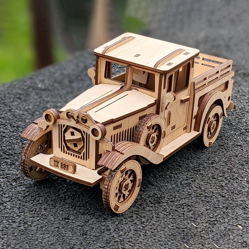 May include: A wooden model kit of a vintage pickup truck. The truck is made of light brown wood and has a detailed design. The truck has a license plate that reads "IX 580".