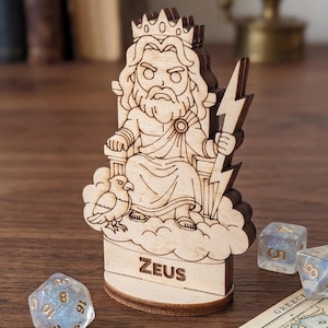 Könnte beinhalten: Holzfigur von Zeus, dem griechischen Gott, der auf einem Thron sitzt und einen Blitz hält. Die Figur hat eine Krone und wird von einem Vogel begleitet. Das Wort "Zeus" steht auf der Basis. Würfel und eine Karte sind im Hintergrund.