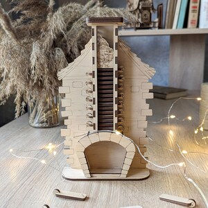 May include: A wooden advent calendar shaped like a house with a chimney and a fireplace. The numbers 11 through 24 are visible on the side of the house. A small figure of Santa Claus is visible in the chimney.