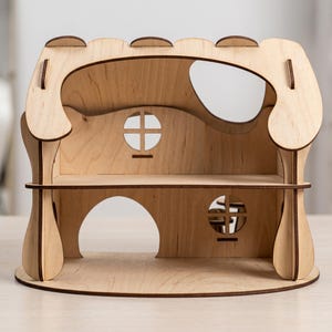 A wooden laser cut dollhouse with a curved roof and two circular windows, sitting on a wooden surface.