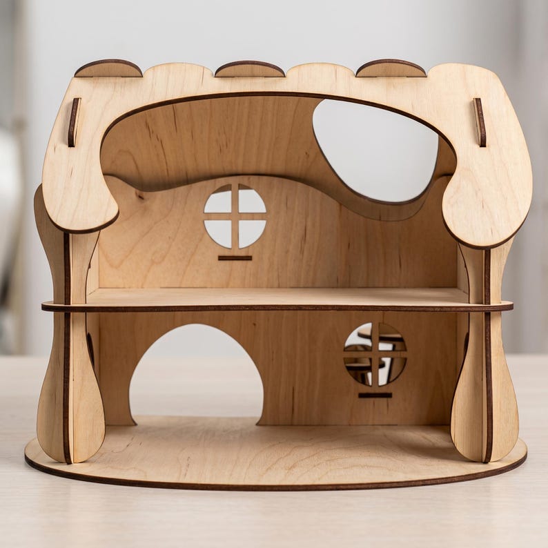 A wooden laser cut dollhouse with a curved roof and two circular windows, sitting on a wooden surface.