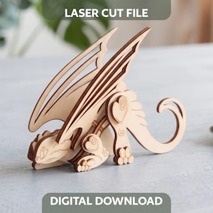 3D laser cut plywood crouching dragon figurine with spread wings on a light grey tabletop near blurred indoor houseplant.