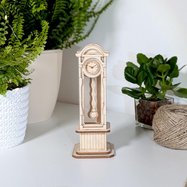 May include: A wooden model of a grandfather clock with a white face and black hands. The clock is standing on a white surface.