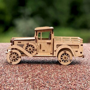 May include: A wooden model of a vintage pickup truck with a brown wood finish. The truck has a flatbed and a detailed cab with a windshield and wheels.
