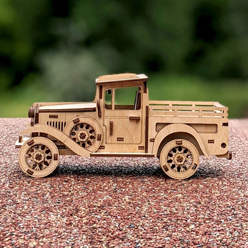 May include: A wooden model of a vintage pickup truck with a brown wood finish. The truck has a flatbed and a detailed cab with a windshield and wheels.