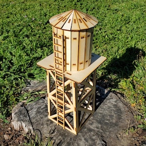 May include: A wooden model of a water tower with a ladder on the side. The tower is made of light brown wood and has a square base. The water tank is cylindrical and has a domed roof.