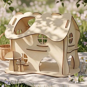 A wooden toy house with a mushroom-like structure on the front, placed on a blanket in a grassy area with flowers.