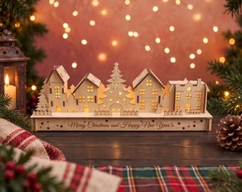 Könnte beinhalten: Ein lasergeschnittenes Weihnachtsdorf aus Holz mit mehreren Häusern, einem zentralen Tannenbaum und einem Zaun. Der Sockel ist mit dem Text Merry Christmas and Happy New Year und kleinen Sternen graviert. Die Struktur ist von innen beleuchtet.
