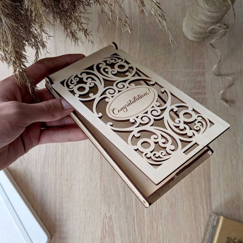 May include: A wooden box with a decorative cutout design and the words "Congratulations!" engraved on the front. The box is open and the lid is folded back.