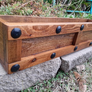 May include: A wooden planter box with a rustic finish and black metal accents. The planter is made of reclaimed wood and has a natural wood grain. It is perfect for adding a touch of rustic charm to any home or garden.