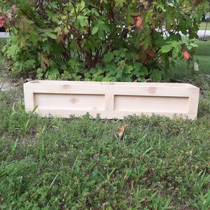 May include: A natural wood planter box with two compartments. The planter is sitting on a bed of green grass.