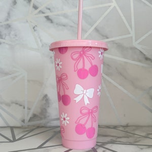 May include: Pink reusable tumbler with a lid and straw. The tumbler features a cherry and bow design.