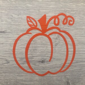 Può includere: Sagoma di zucca arancione con gambo e foglia, su uno sfondo di legno.