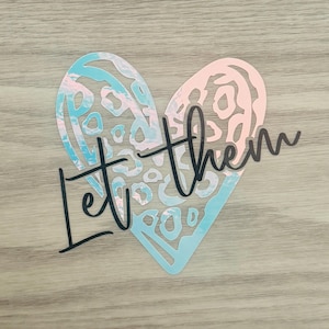 May include: A blue and pink heart-shaped design with a white and black leopard print pattern. The text "Let them" is written in black cursive script below the heart.