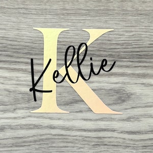 Puede incluir: Una letra K dorada con el nombre Kellie escrito en cursiva negra.