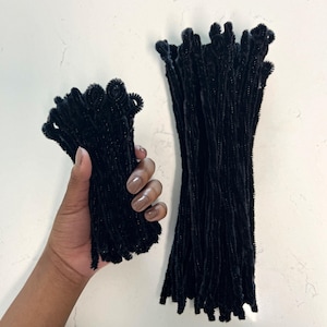 May include: Two bundles of black pipe cleaners. One bundle is held in a hand, the other is lying flat on a white surface.