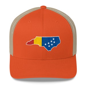 May include: A trucker hat with a mesh back in a light brown colour. The front of the hat is orange and features an embroidered design of the state of North Carolina with the state flag colours.
