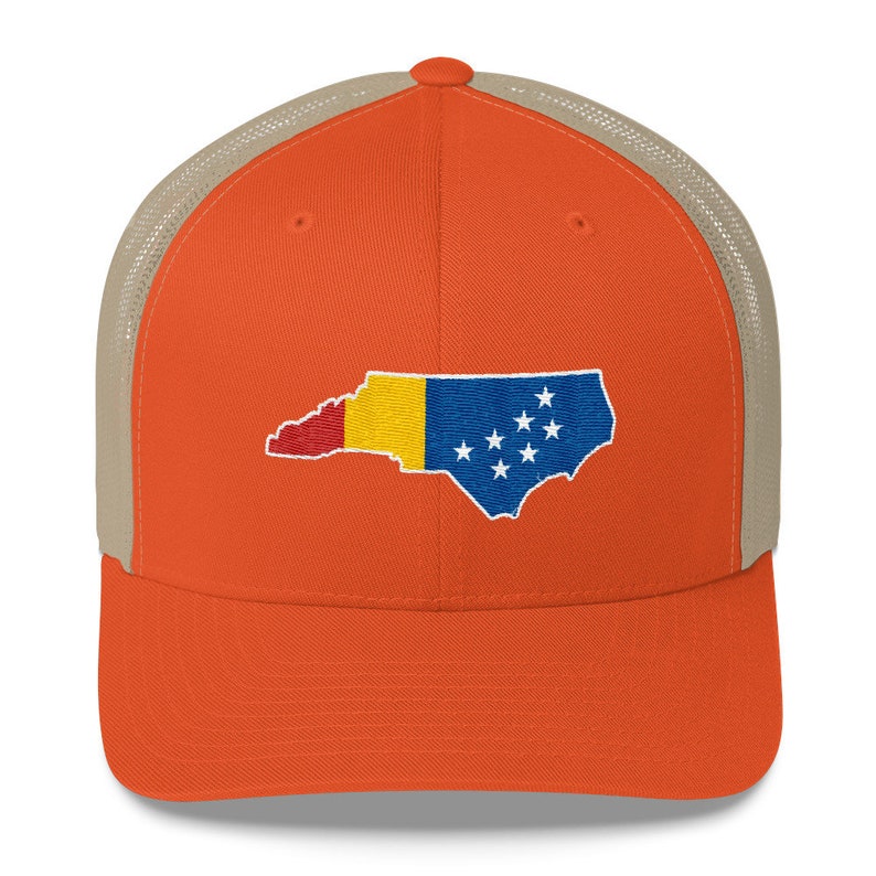 May include: A trucker hat with a mesh back in a light brown colour. The front of the hat is orange and features an embroidered design of the state of North Carolina with the state flag colours.