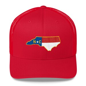 May include: Red trucker hat with a mesh back. The hat features an embroidered outline of the state of North Carolina with the state flag colors and the letters "N*C" in the center.