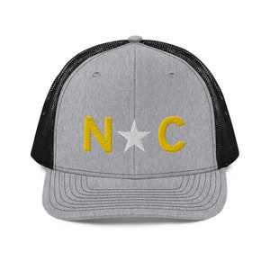May include: A gray and black trucker hat with a white star and the letters "N*C" embroidered in yellow.