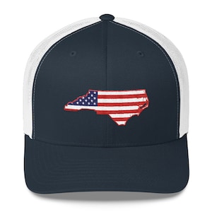 May include: A navy blue and white trucker hat with a white mesh back. The front of the hat features an embroidered outline of the state of North Carolina with the American flag inside.