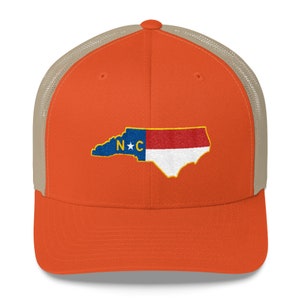 May include: Orange and tan trucker hat with an embroidered North Carolina state outline and flag. The flag has a blue field with a white star and the letters "N*C" in white. The outline of the state is in white.