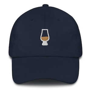 Peut inclure: Casquette de baseball bleu marine avec un motif brodé blanc d'un verre à whisky. Le verre est rempli d'un liquide brun. La casquette a une visière incurvée et un bouton sur le dessus.
