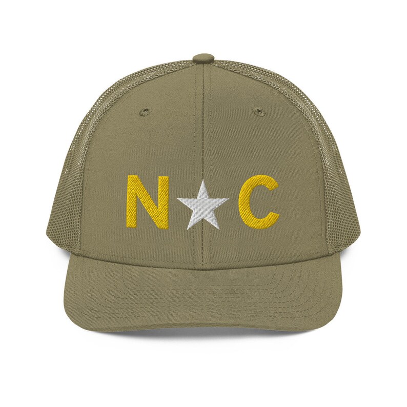 May include: A khaki green trucker hat with a mesh back. The front of the hat has a white star and the letters "N*C" in yellow embroidery.