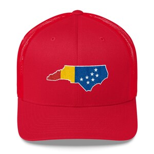May include: Red mesh trucker hat with an embroidered outline of the state of North Carolina in the colours of the North Carolina flag.