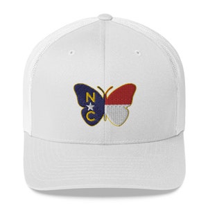 May include: White trucker cap with a mesh back and a curved peak. The front displays an embroidered butterfly design in the colours of the North Carolina state flag. The butterfly design is split down the middle.