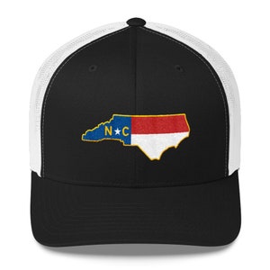 May include: A black and white trucker hat with a mesh back. The front of the hat features an embroidered outline of the state of North Carolina with the state flag colours and the letters "N*C" in the centre.