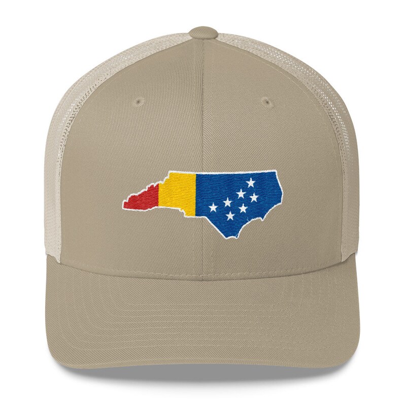 May include: A beige and white trucker hat with an embroidered outline of the state of North Carolina, filled with the colours of the North Carolina flag.