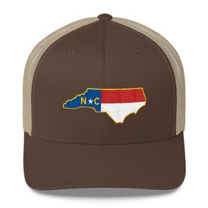 May include: A brown and tan trucker hat with a brown brim and a mesh back. The hat features an embroidered image of the state of North Carolina with the letters "N*C" in the center.
