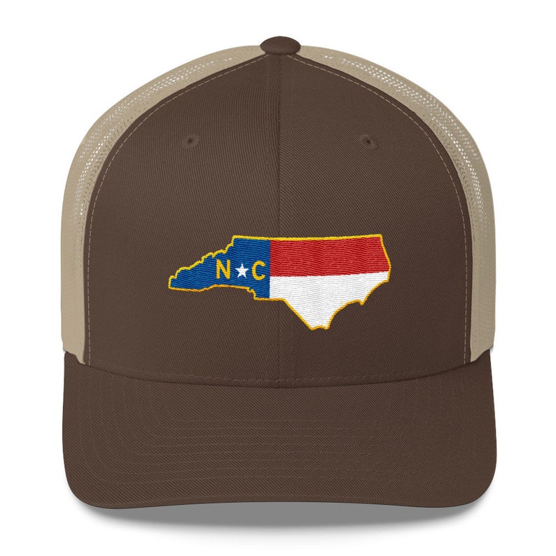 May include: A brown and tan trucker hat with a brown brim and a mesh back. The hat features an embroidered image of the state of North Carolina with the letters "N*C" in the center.