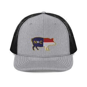 May include: Gray trucker hat with a black mesh back and a curved brim. The front features an embroidered pig design with the North Carolina state flag colors and the letters "NC".