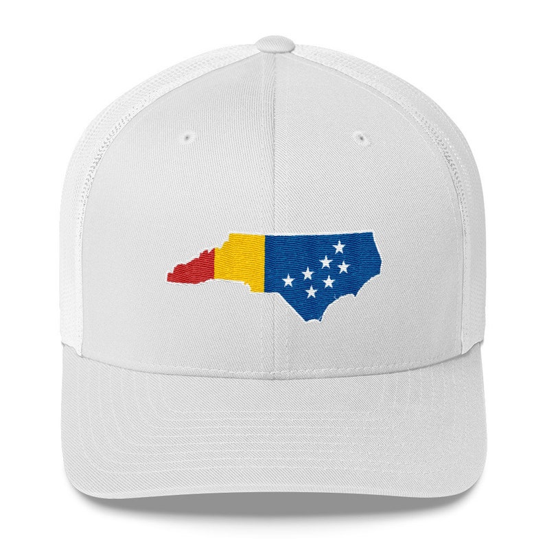 May include: White trucker hat with a white embroidered outline of the state of North Carolina, filled with the colours of the Romanian flag. The hat has a mesh back.