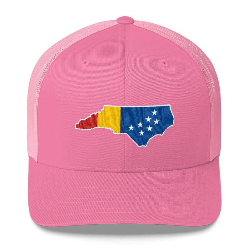 May include: Pink trucker hat with a mesh back. The hat features an embroidered design of the state of North Carolina with the colours of the Romanian flag.