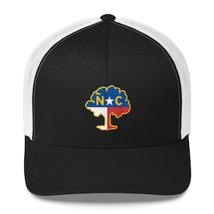 May include: A black and white trucker hat with a black front panel and a white mesh back panel. The front panel features an embroidered design of a tree with the letters "N*C" on the trunk. The tree is in the colours of the North Carolina state flag.