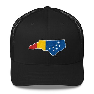 May include: Black trucker hat with a mesh back. The front of the hat features an embroidered outline of the state of North Carolina with the state flag colours.