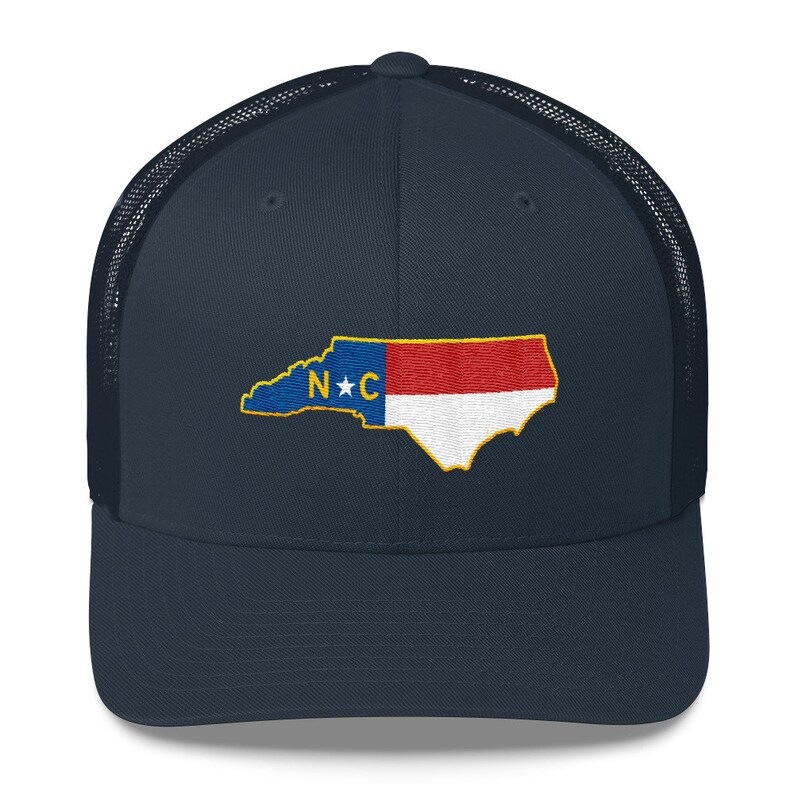May include: A navy blue trucker hat with a mesh back. The front of the hat features an embroidered design of the state of North Carolina with the state flag colors and the letters "N*C" in the center.
