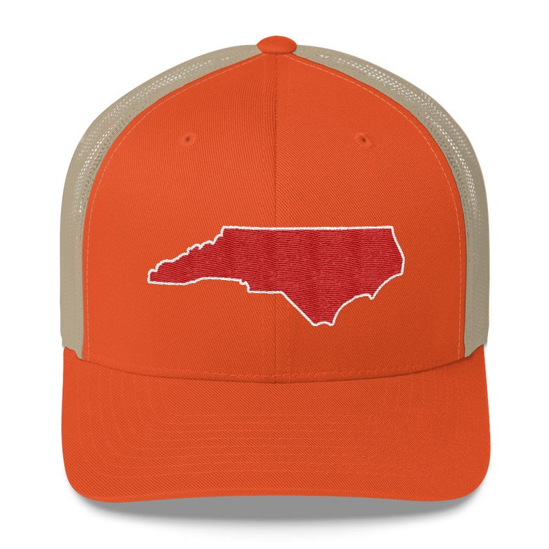 Pu&ograve; includere: Un cappello da camionista con una parte posteriore in rete color beige e un pannello anteriore arancione. Il pannello anteriore presenta un contorno ricamato rosso dello stato della Carolina del Nord.