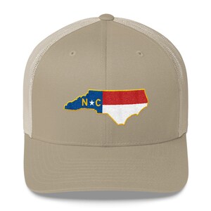 May include: A beige and black trucker hat with an embroidered North Carolina state outline and flag. The flag is red, white, and blue with a blue star and the letters "N*C" in the center.